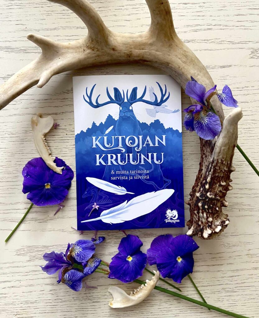 Kutojan kruunu teos pöydällä koristeellisen peuransarven ja sinisten kukkien ympäröimänä
